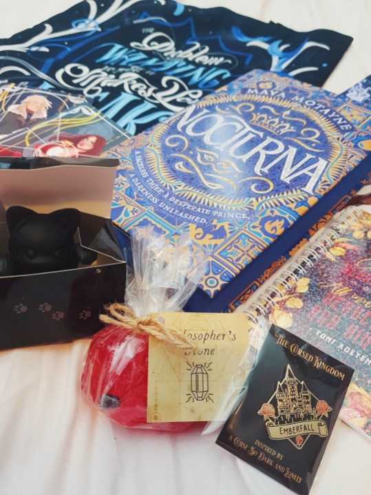 Fairyloot April Dark Magic unboxing photograph - features leigh bardugo (tote bag) and jay kristoff (black cat tea strainer) inspired merch, along with a philosophers stone soap.